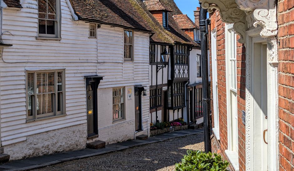 A narrow residential street in Addington with a cobblestone pavement and brick terraced houses on both sides. On the right, a row of red-brick houses features white-framed sash windows and individual 